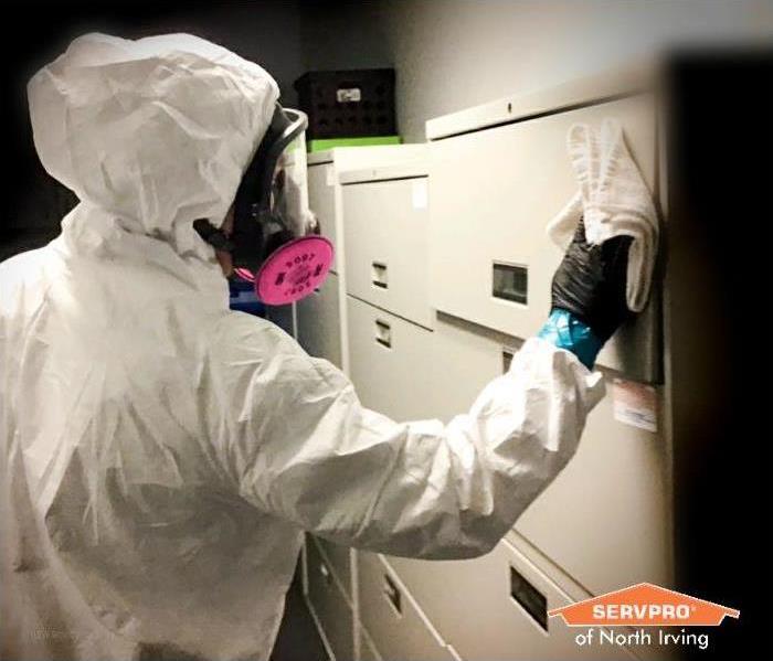 SERVPRO technician in white coveralls and a full face mask wiping down a filing cabinet